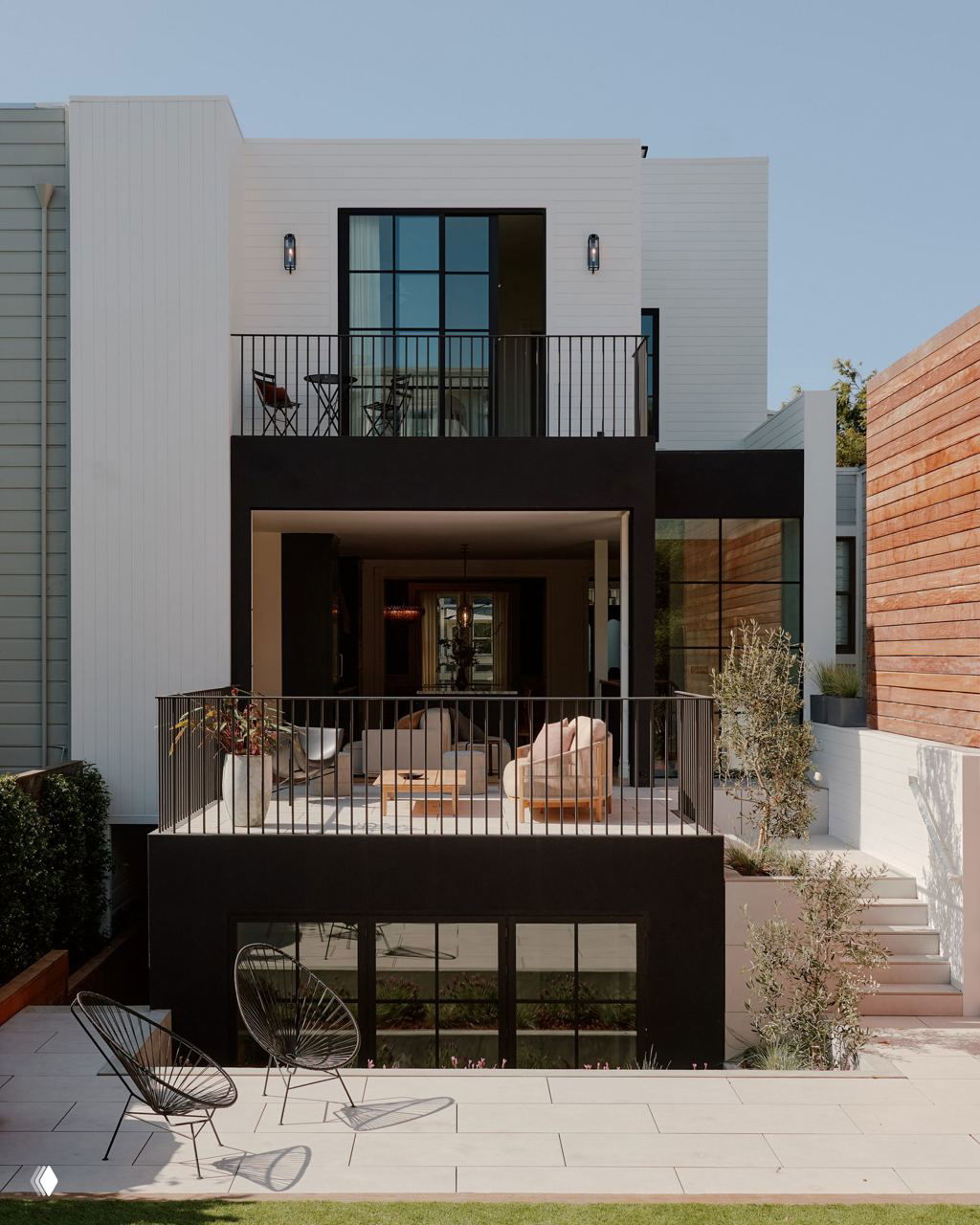 Задняя часть дома с открытой террасой и балконом: контрастные черные рамки, уличная мебель и панорамные стеклянные окна в современном ключе.