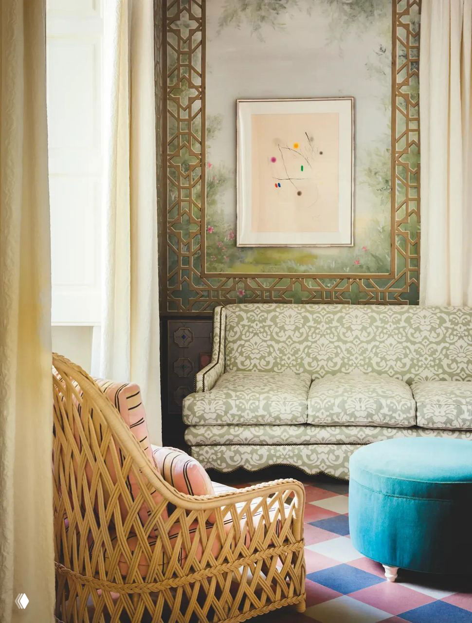 Интерьер гостиной бутик-отеля Фрэнсиса Форда Копполы в Бернальде: плетёное кресло, узорный диван и бирюзовый пуф на фоне воздушной фрески и высоких штор.