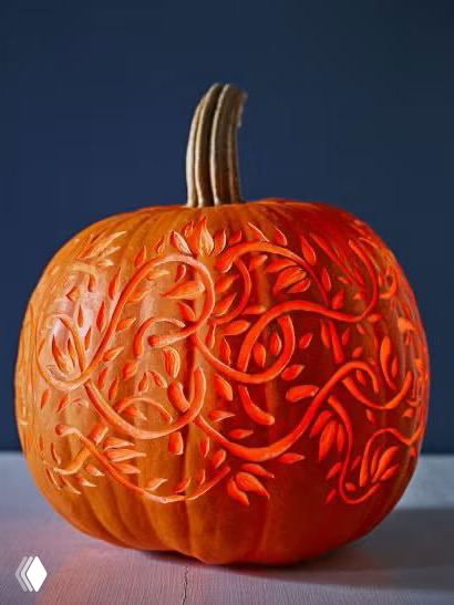 Тыква с тонкой декоративной резьбой в виде растительных узоров, крупный план демонстрирует сложную работу ножом и эффект рельефа на поверхности кожуры, акцент на мастерстве.