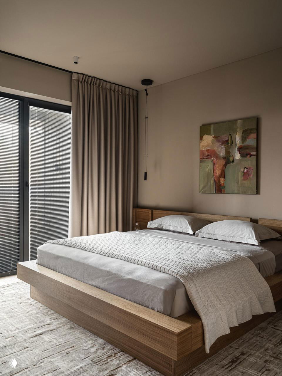 Спальня с низкой деревянной кроватью, спокойной пастельной постелью и абстрактной картиной над изголовьем — теплые естественные оттенки интерьера.