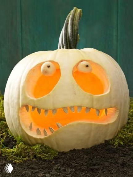 Бледная белая тыква с круглыми глазами и зубастым ртом, подсвеченная изнутри; изображение показывает фактуру поверхности и контраст между светом и темной почвой рядом.