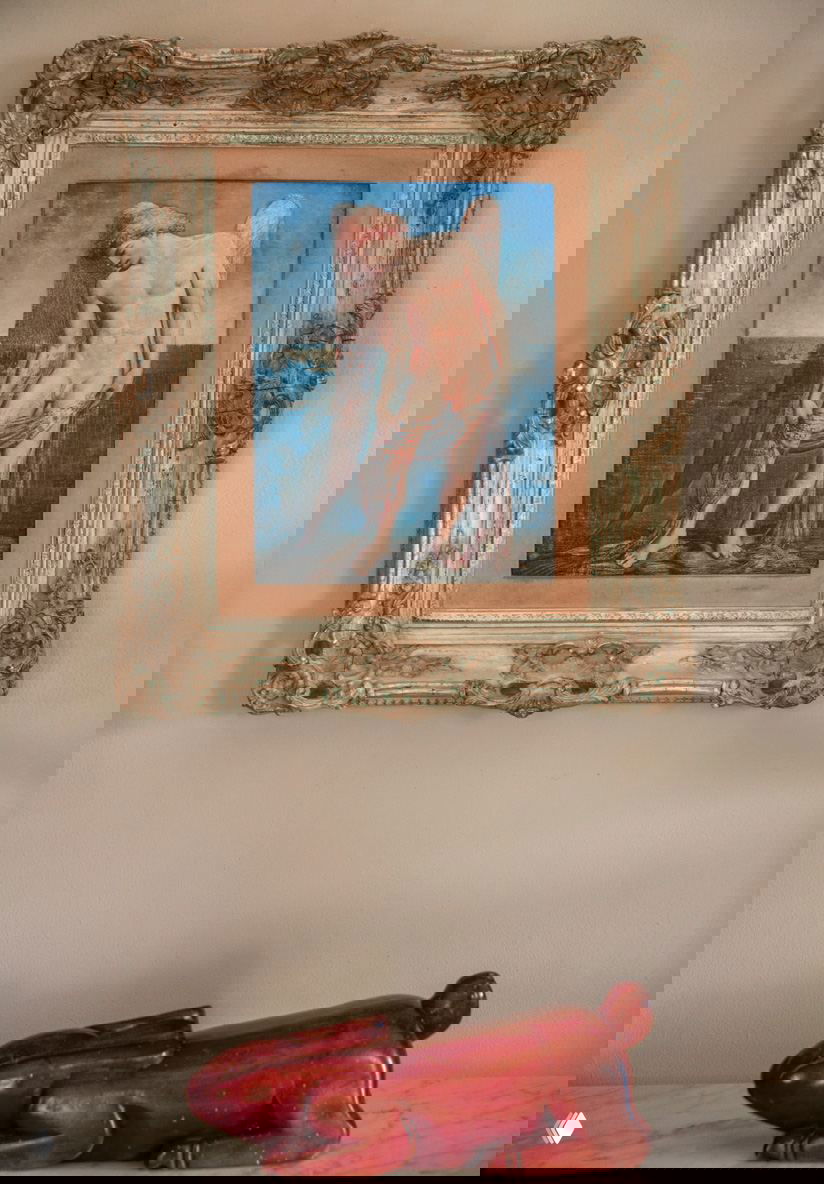 Картина в резной золотой раме и небольшая декоративная скульптура на столе в доме в Доминикане, часть художественной коллекции интерьера.