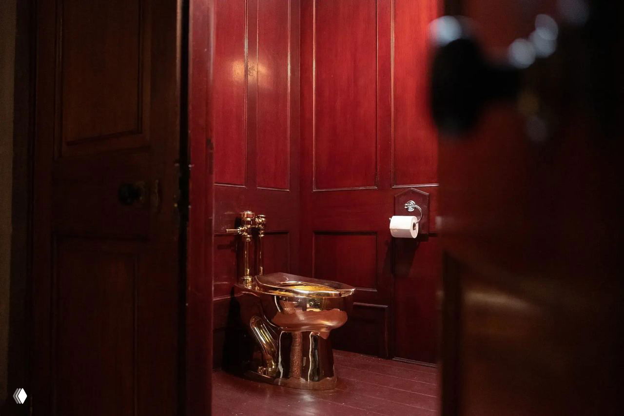 Фотография золотого унитаза Маурицио Каттелана в помещении с тёмно-красными деревянными панелями — вид через приоткрытую дверь, интерьерный кадр.