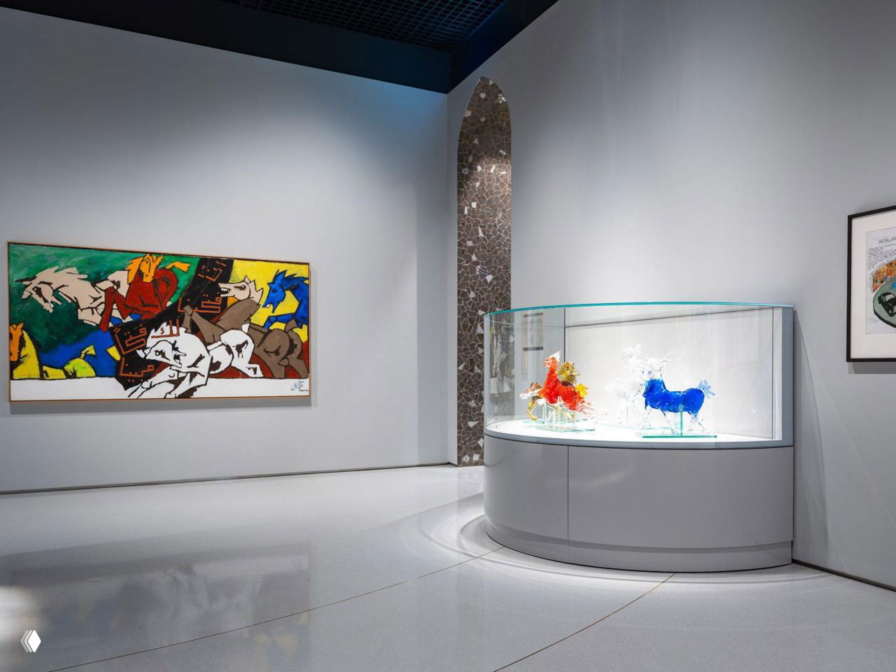 Интерьер выставочного зала музея: белые стены, витрина со стеклянными скульптурами и большая живописная работа на стене слева.