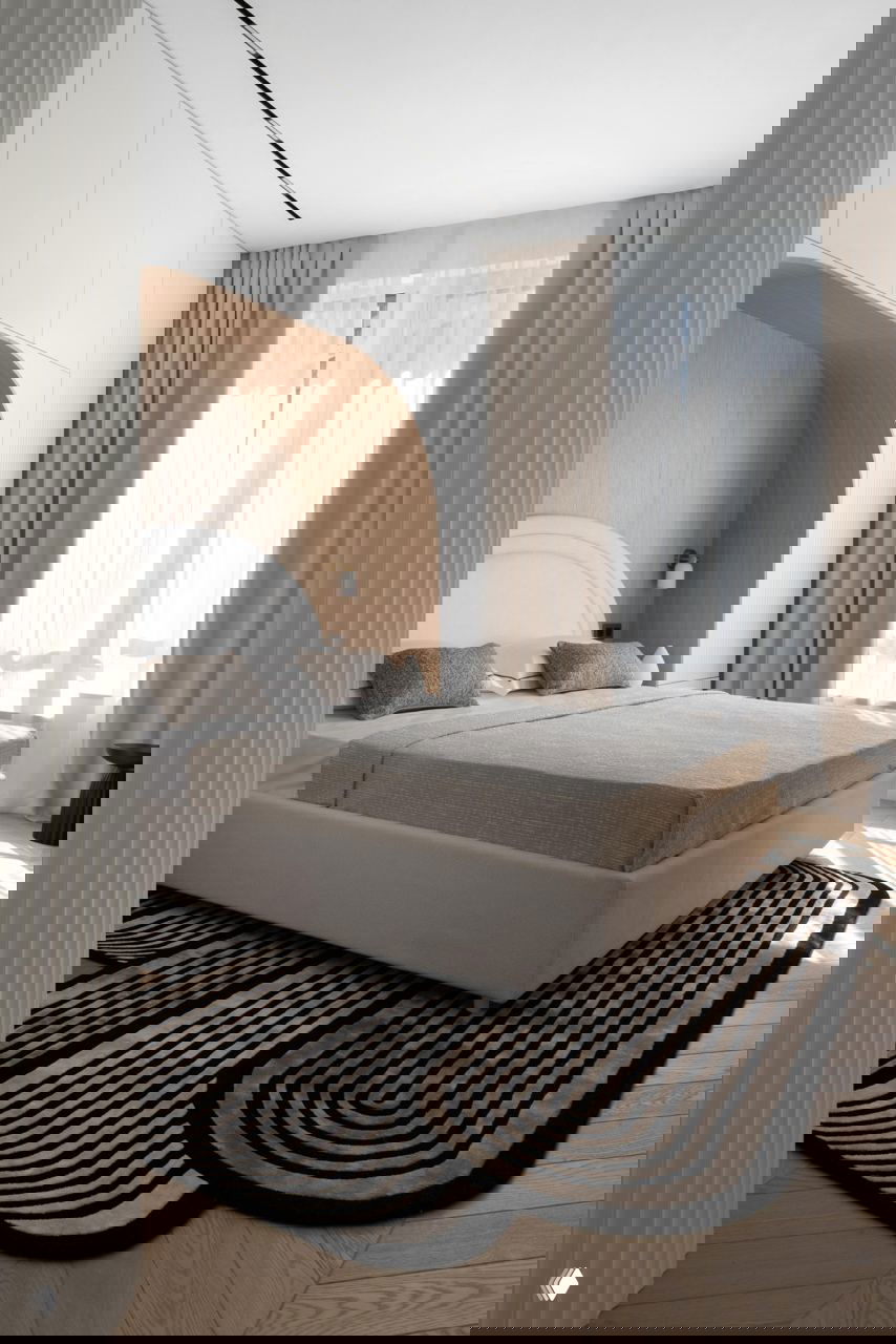 Спальня с нишей из шпона: кровать в бежевых тонах и крупный декоративный ковёр в чёрно-белую графику, создающий мягкий акцент в комнате.