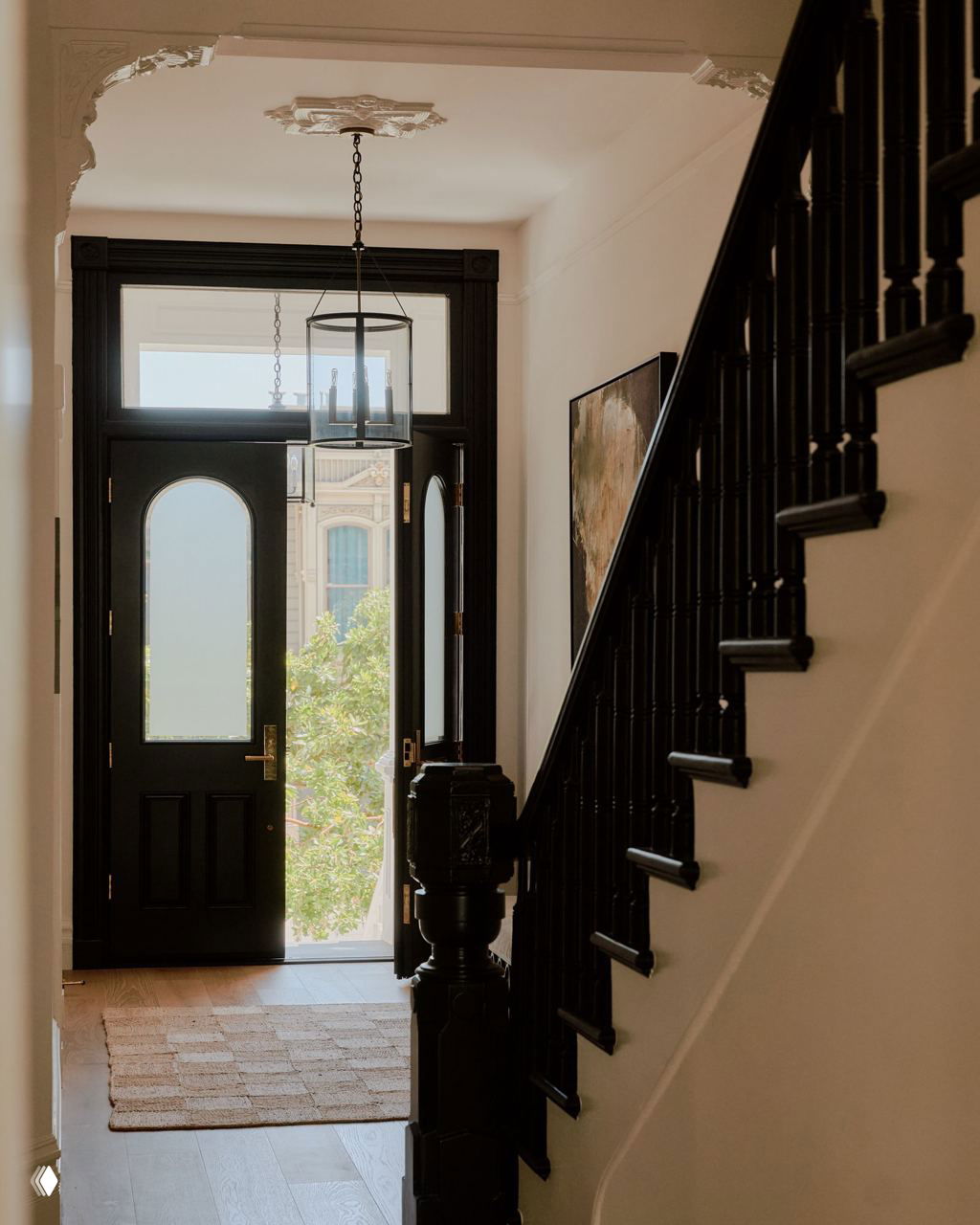 Прихожая с чёрной входной дверью и лестницей с тёмными перилами, украшенная лепниной и мягким дневным освещением — связь исторического и современного.