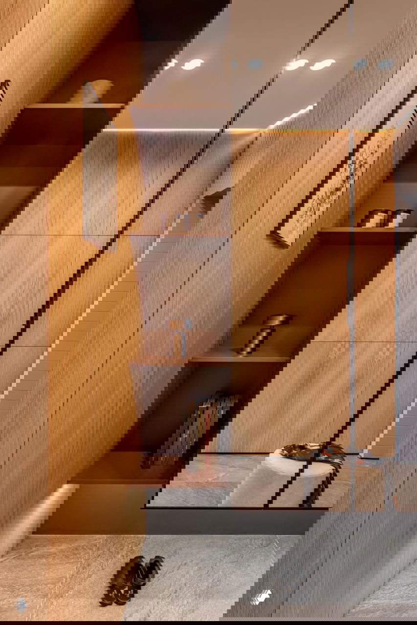 Фрагмент гардеробной ниши с открытыми полками, встроенной подсветкой и теплыми деревянными панелями, зеркальная поверхность визуально расширяет пространство.