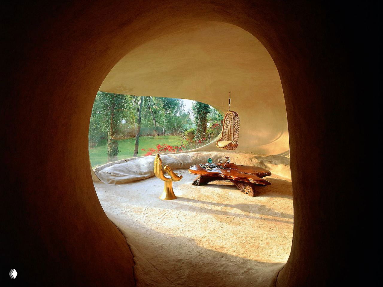 Интерьер через округлый проем: мягкие бетонные поверхности, низкие линии и столовая зона с необычной мебелью внутри Casa Organica.