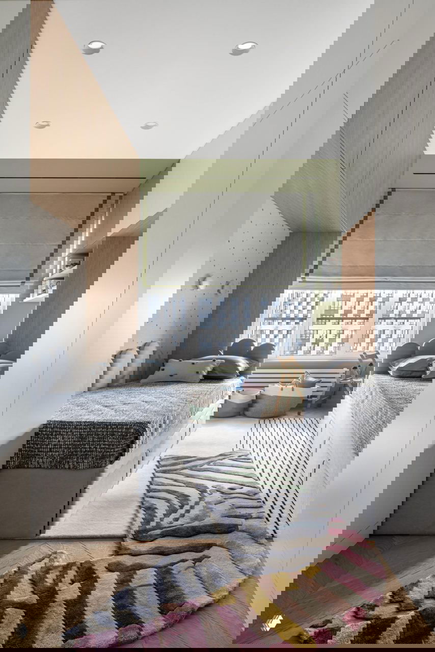 Детская комната для двух детей: пара однотипных спальных мест, игровой ковёр со сложным орнаментом и встроенные шкафы для удобного хранения вещей семьи.