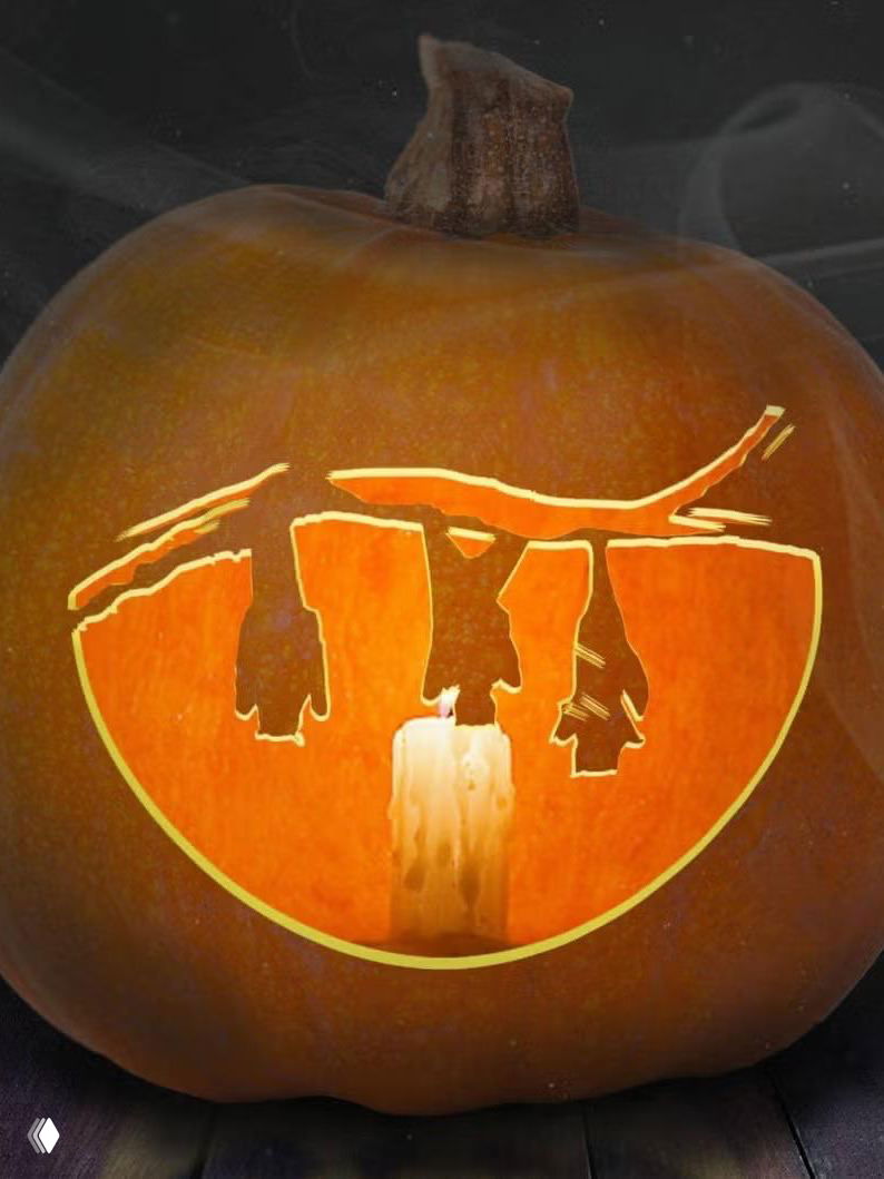 Крупный план вырезанного сюжета в тыкве с силуэтом фигур над свечой внутри; композиция создаёт драматический светотеневой эффект и интересную игру силуэтов.