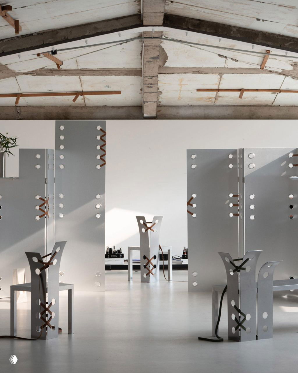 Инсталляция скульптурной мебели Pul Нары Ли в светлом зале: металлические панели и стулья с кожаными ремнями на фоне потолка и окон выставочного пространства.
