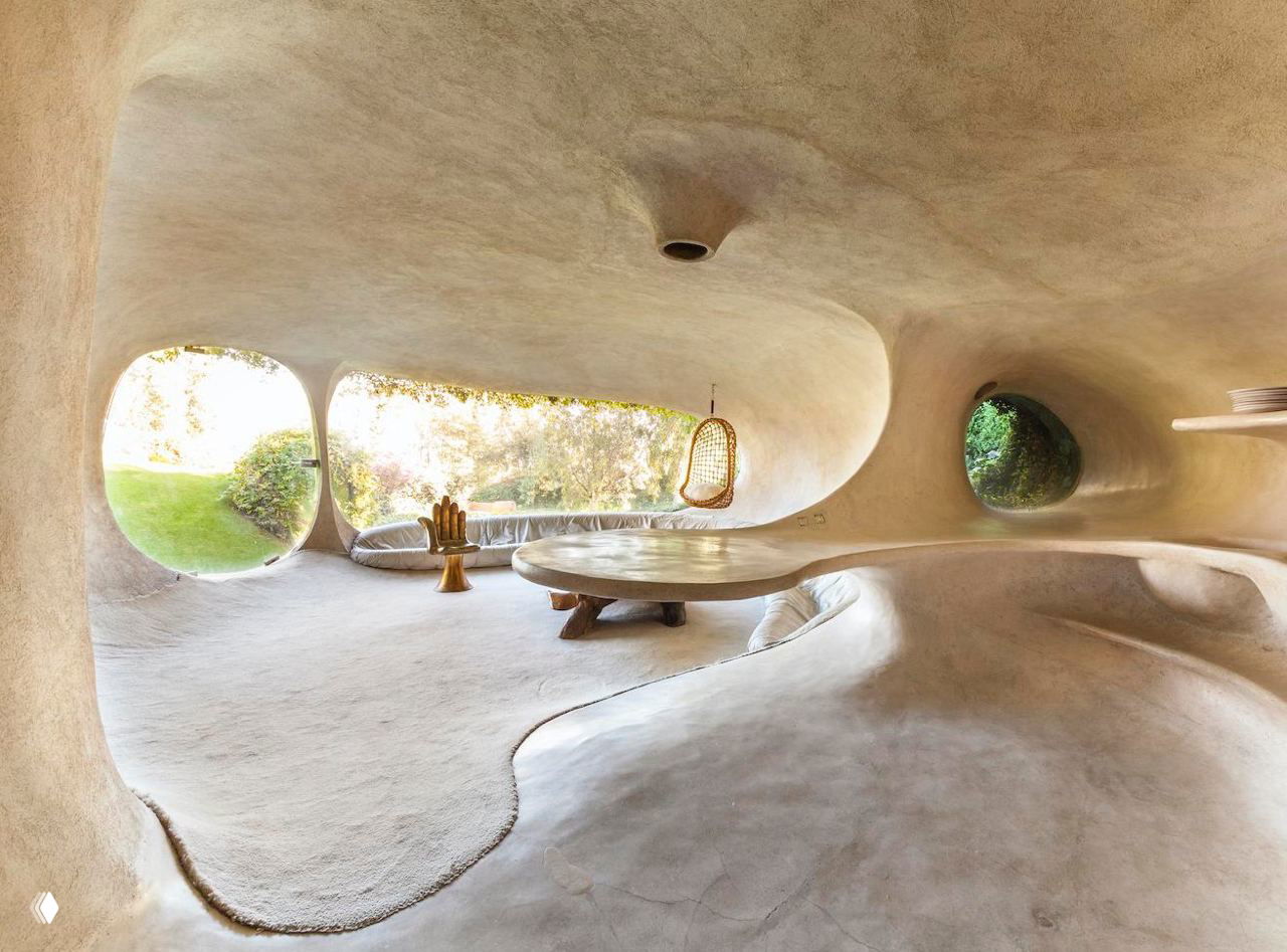 Широкий внутренний зал с большими овальными окнами на сад, полукруглыми сиденьями и качающимся плетеным креслом у проема.