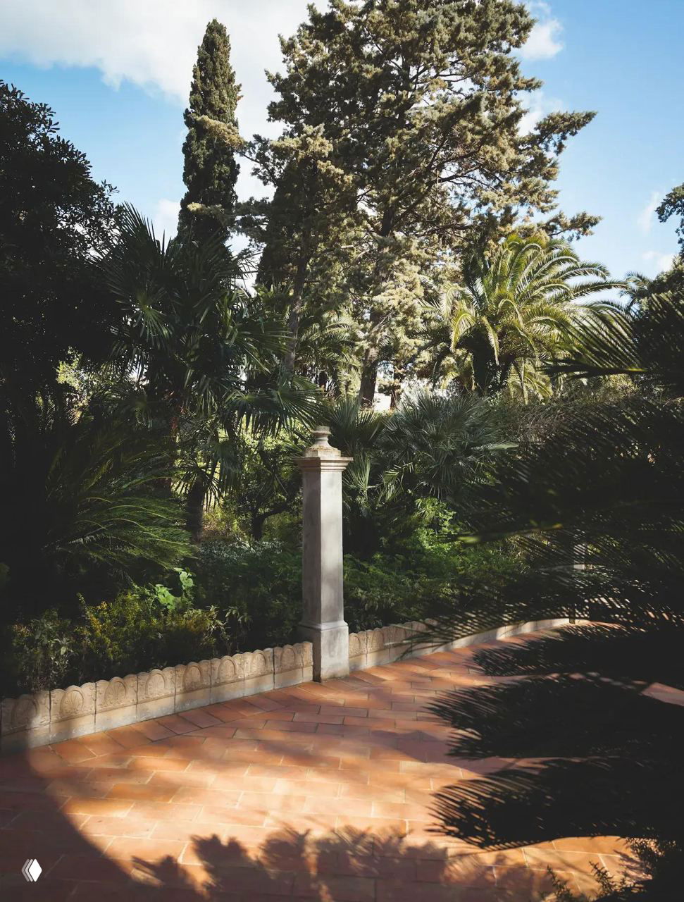 Сад и терраса палаццо с средиземноморской растительностью: пальмы и кипарисы, терракотовая плитка и дорожки, создающие атмосферу юга Италии вокруг отеля-дома Копполы.