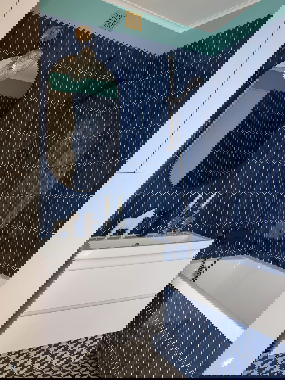 Ванная комната с насыщенно-синими вертикальными плитками, белой сантехникой и геометрической черно-белой напольной плиткой — ретро-нотки в сантехнике.