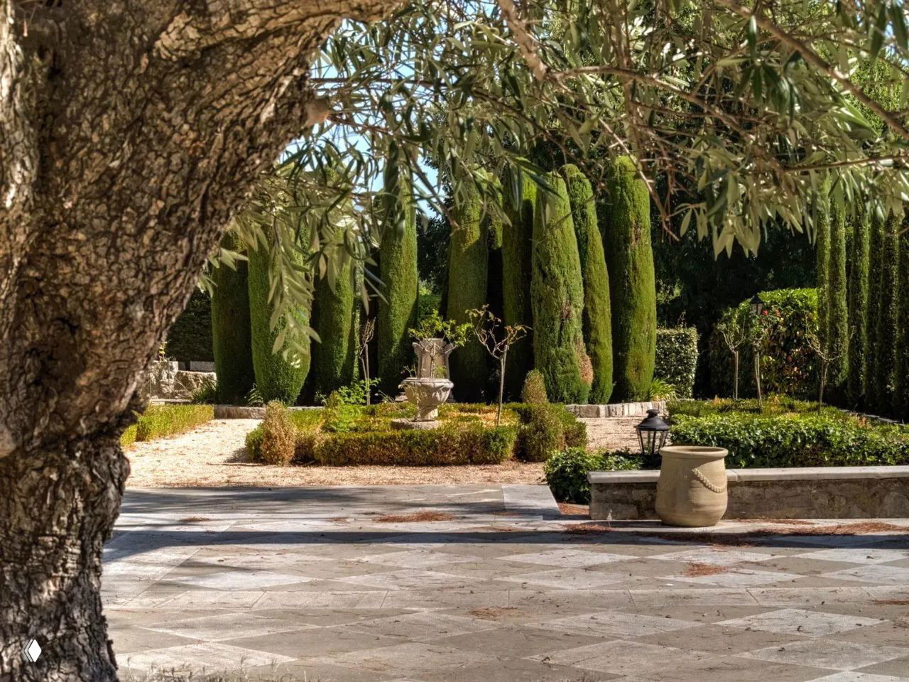 Фрагмент французского регулярного сада с кипарисами, декоративными вазонами и симметричными посадками на фоне аллей.