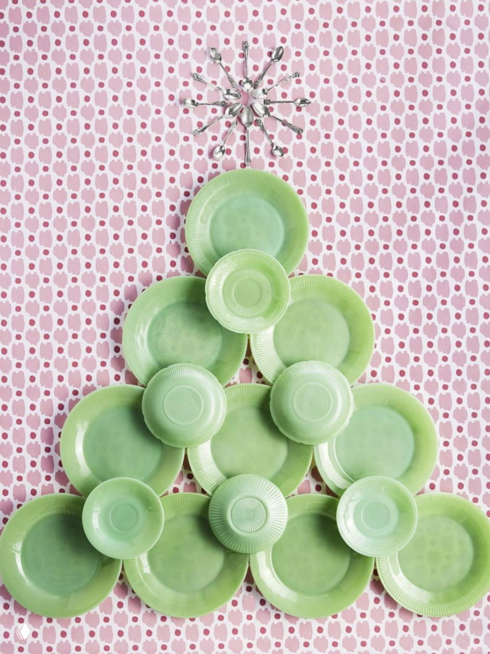 Настенная композиция в виде ёлки из светло‑зелёных керамических тарелок на фоновых розово‑белых обоях — креативная идея для праздничного декора.
