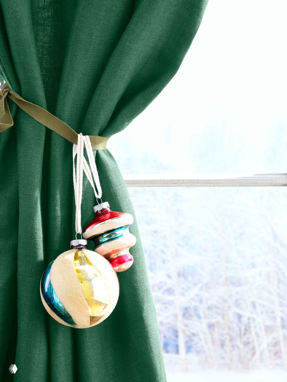 Пара винтажных стеклянных шаров, подвешенных на ленту подхвата для штор у зелёной ткани у окна — идея использовать шторный подхват для украшений.