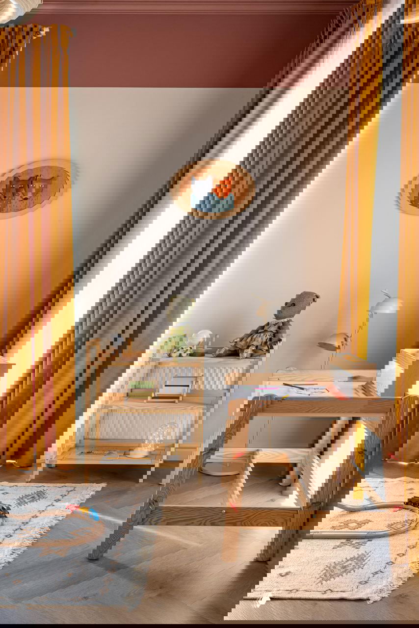 Детская игровая зона у окна с жёлтыми шторами, деревянной мебелью и ковриком — пространство организовано для ребёнка и гармонично вписано в интерьер.