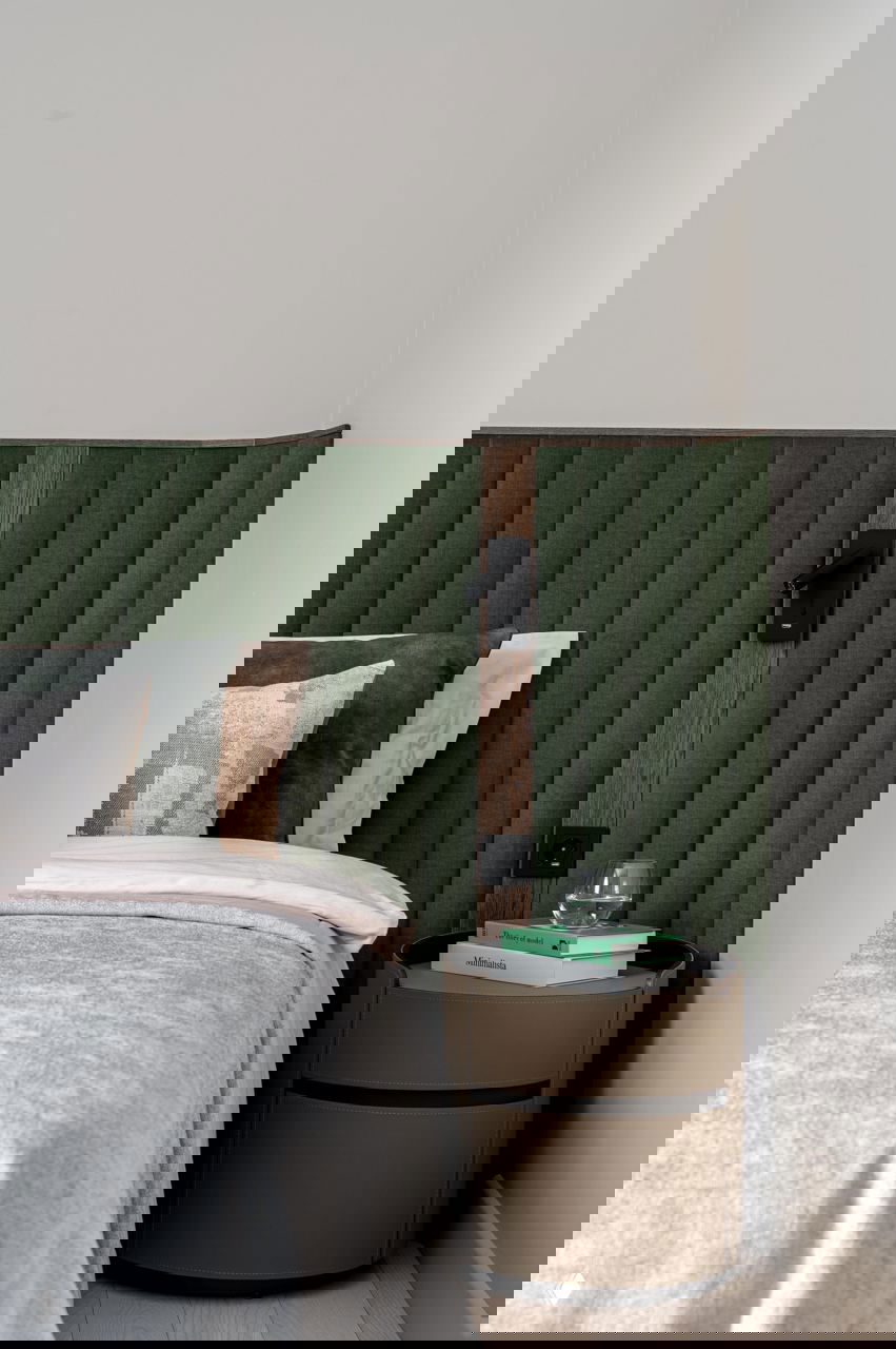 Крупный план изголовья кровати с вертикальной стёжкой и прикроватной тумбой; демонстрация фактур и функциональных светильников.