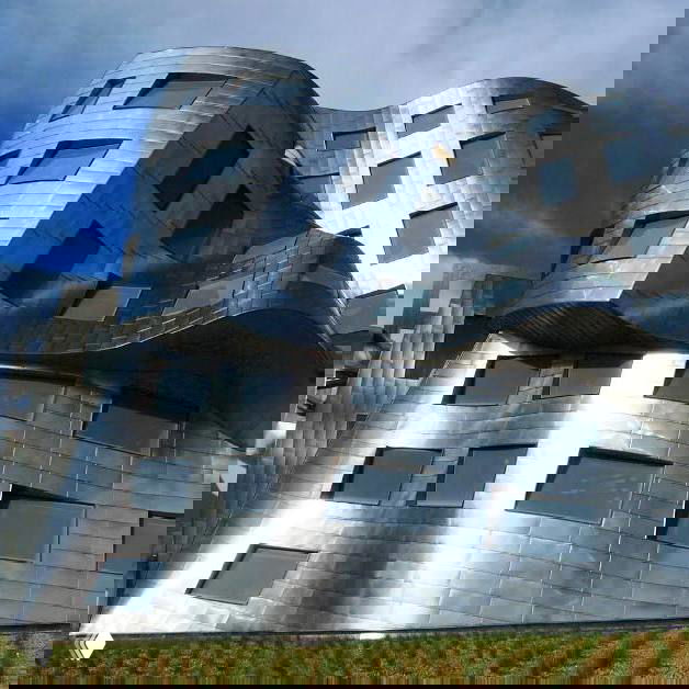 Ближайний план изгибающейся металлической оболочки здания с квадратными окнами — характерный мотив в работах Гери.