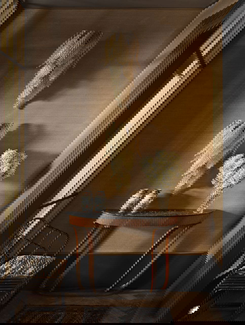 Интерьер торца коридора: тонкая консоль с мраморной столешницей, настенные бра в виде листьев и изящные декоративные вазочки на фоне ламповых оттенков стены.