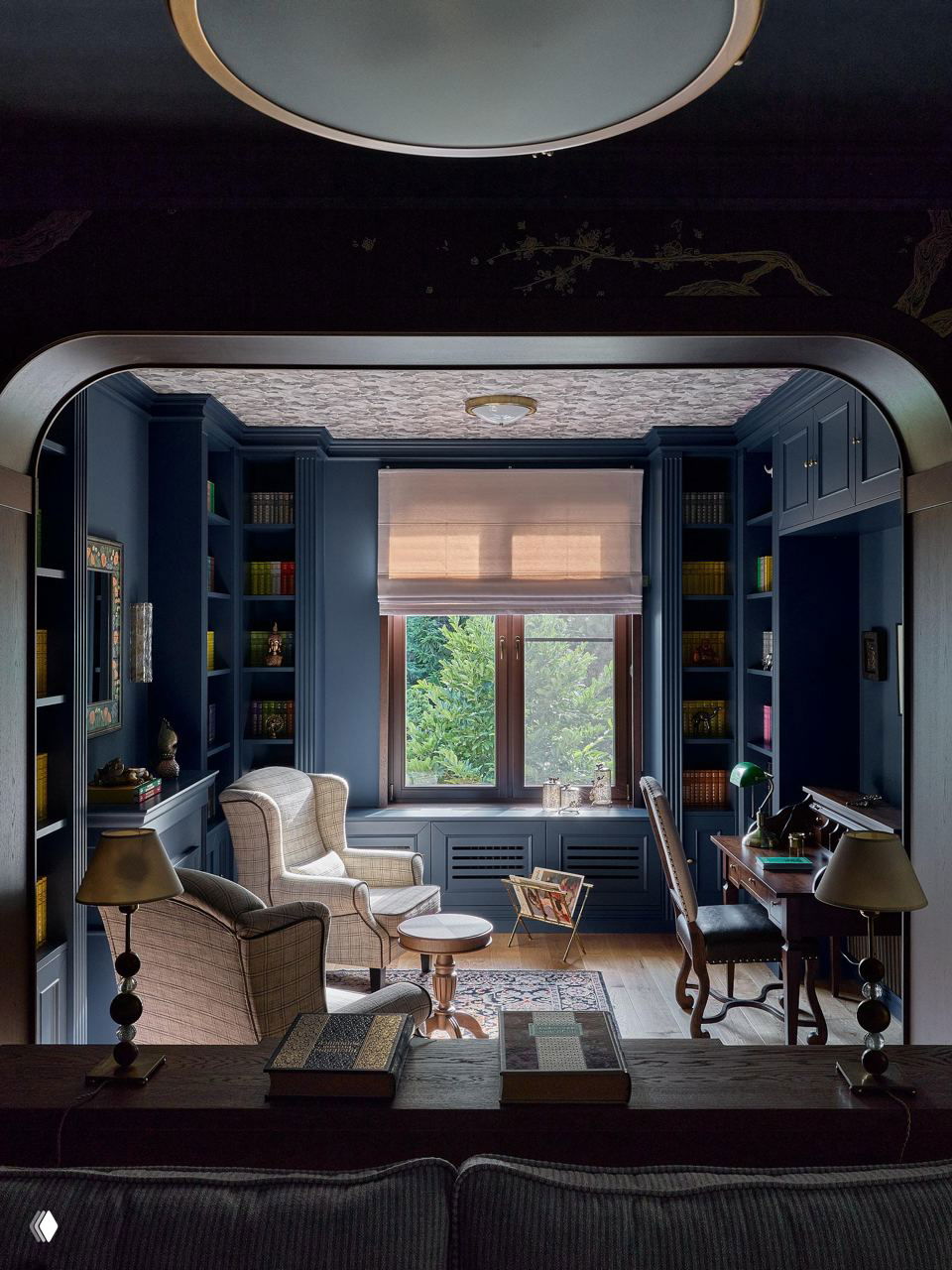 Вид комнаты с арочным проёмом: окно с видом на зелёный сад, книжные полки, рабочее место и уютная зона для чтения в классическом стиле.