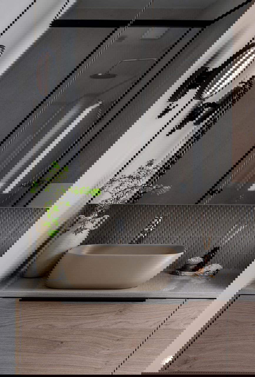 Ванная комната с бежевой чашей раковины, зеркалом и зелёными растениями; спокойная натуральная палитра в сантехнической зоне.