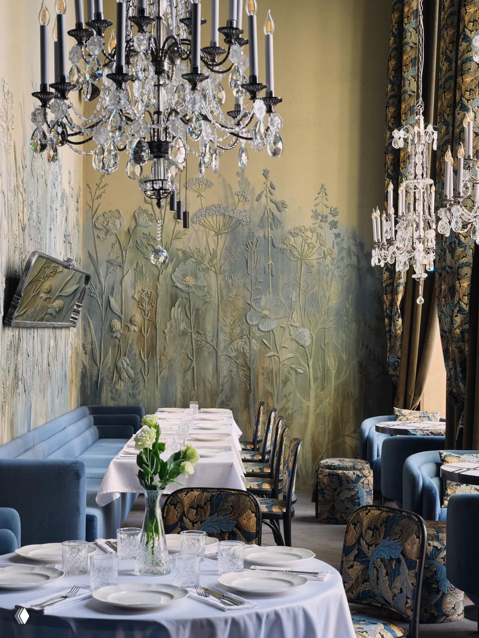 Банкетный зал с декоративными настенными панно, хрустальными люстрами и столами, накрытыми белыми скатертями и фарфором.