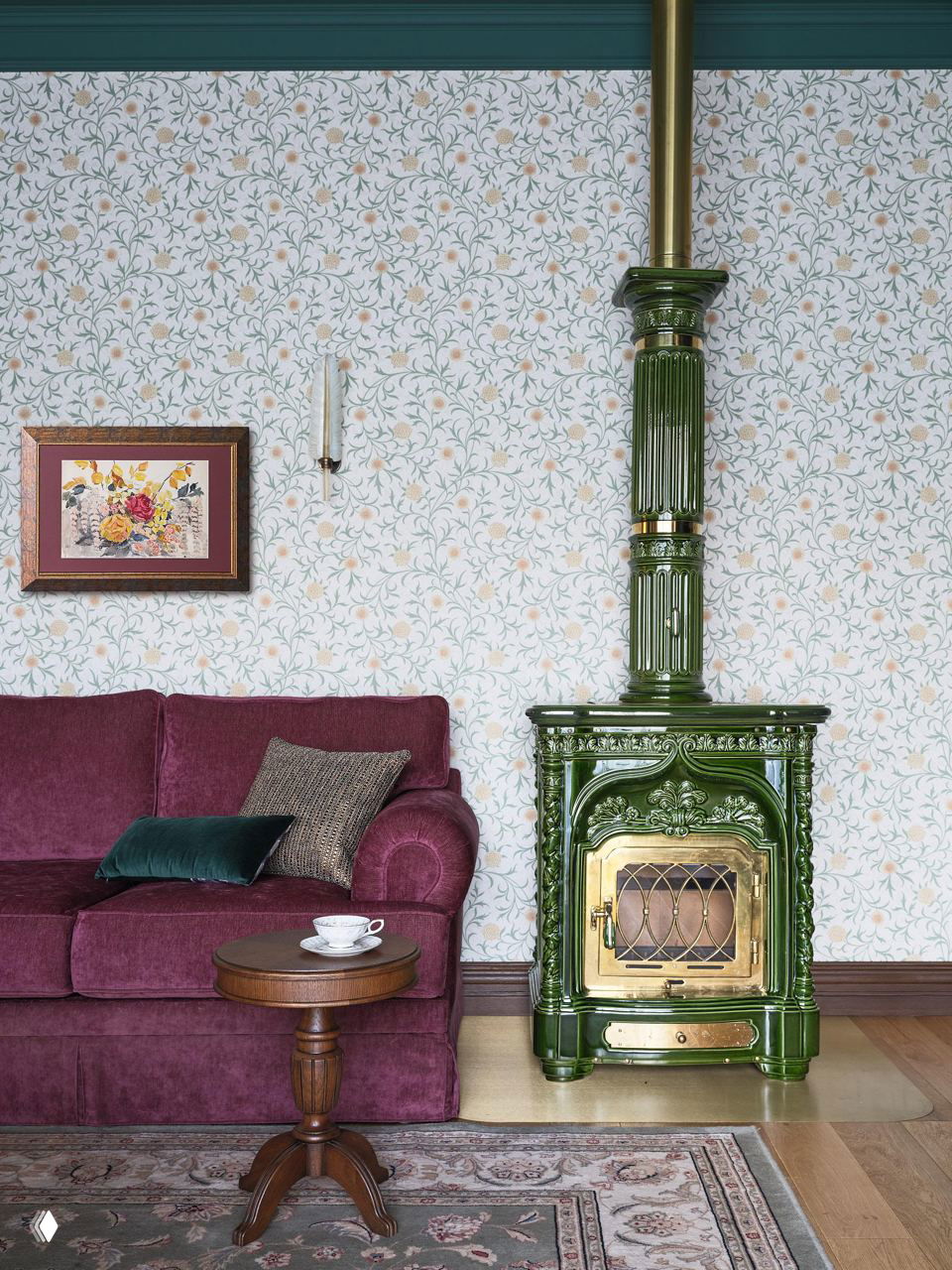 Угол гостиной с зелёной эмалированной печью-камином, бархатным диваном винного оттенка и декоративным ковром на деревянном полу.