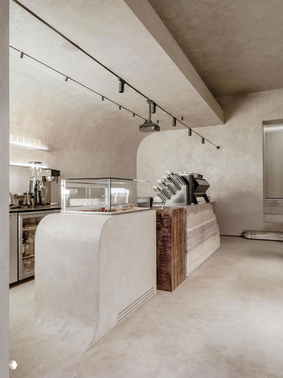 Вид на барную зону St.Riders Coffee: закруглённая стойка из микроцемента, деревянные вставки и нержавеющая сталь в тёплой серой палитре.