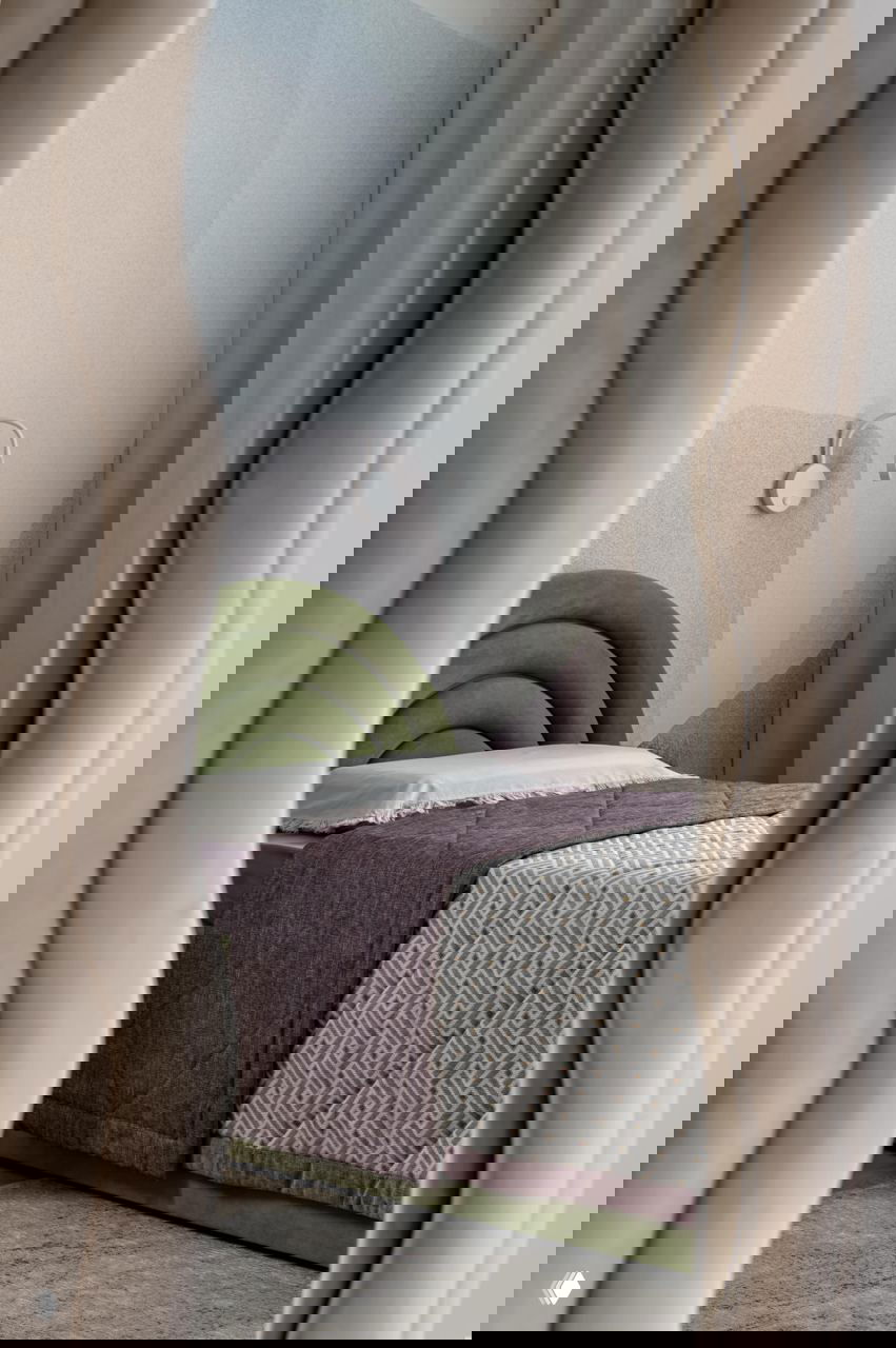 Детская комната с мягкой волнообразной кроватью, пастельными и зелёными акцентами; отражение в декоративном зеркале подчёркивает интерьер.