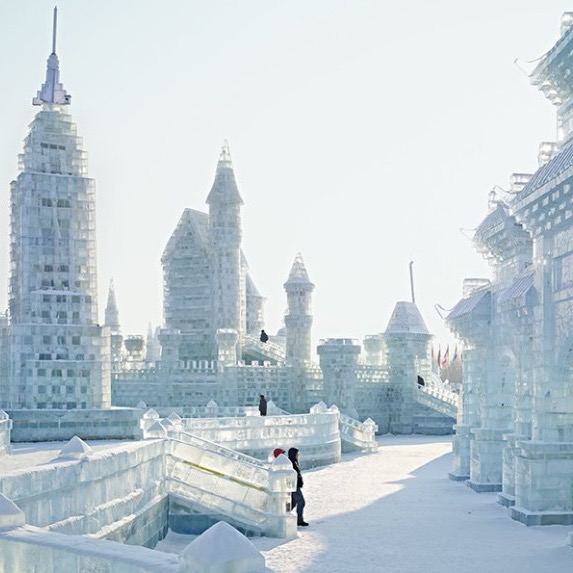 Панорамный вид на ледяные замки и стены фестиваля в Харбине, прогулки посетителей на фоне прозрачных ледяных конструкций.