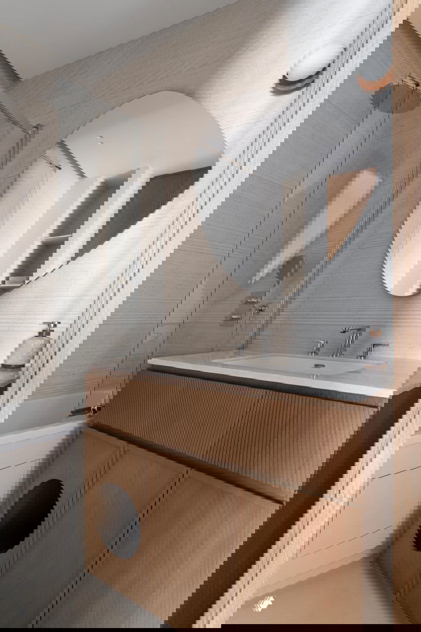 Ванная комната с деревянной тумбой под раковиной и большим овальным зеркалом; в фасаде тумбы заметно круглое отверстие, интегрированное в дизайн.