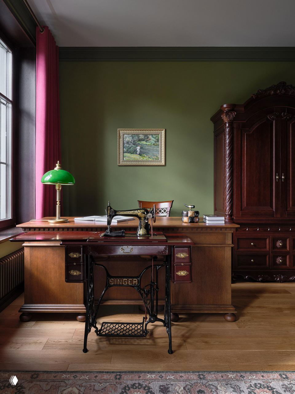 Рабочий кабинет с массивным деревянным столом, старинной швейной машиной Singer в подставке и зелёными стенами в тёплой палитре.