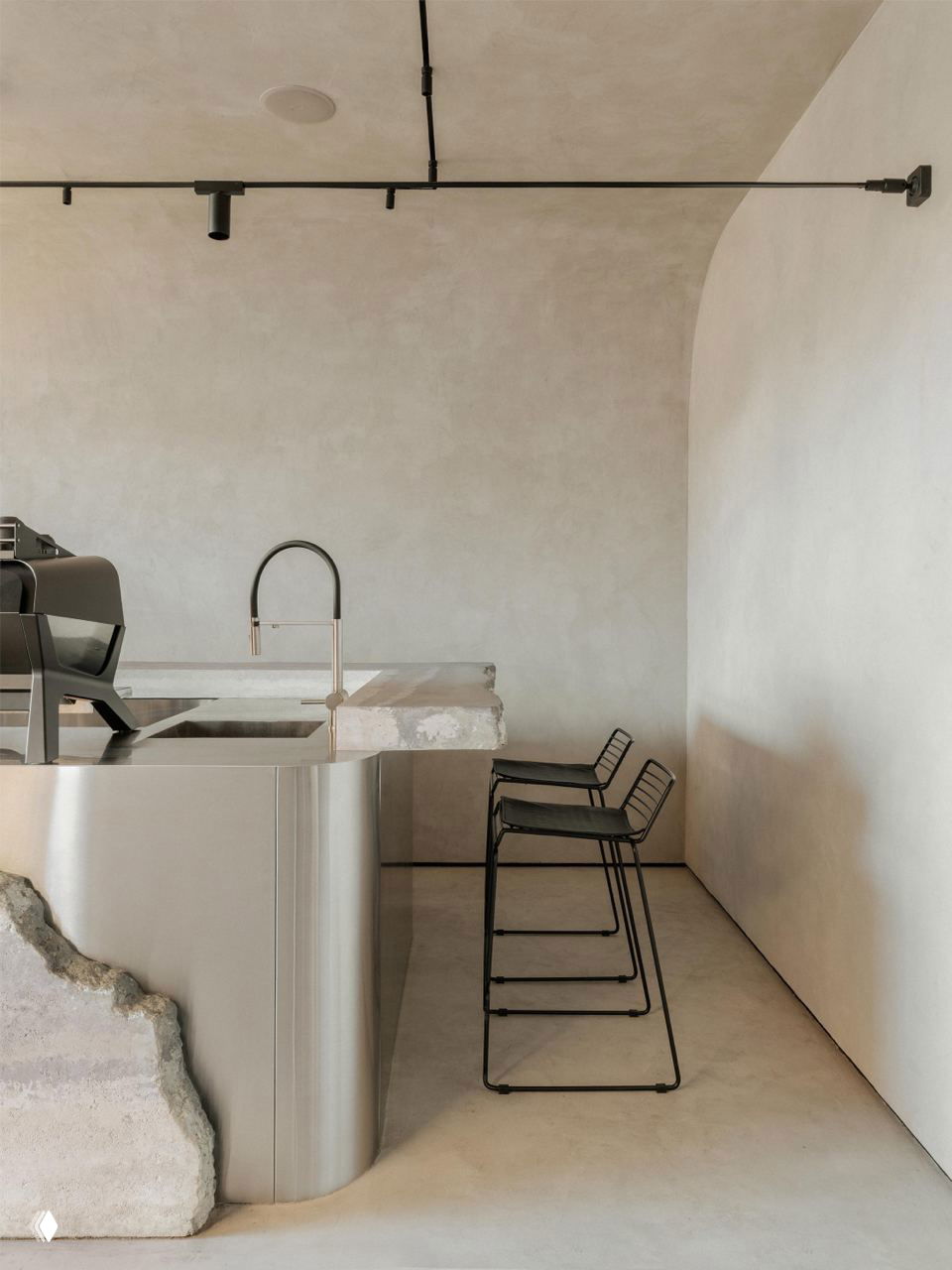 Угловая часть бара и три металлических барных стула на фоне светлых микроцементных стен с плавным переходом потолка в стену.