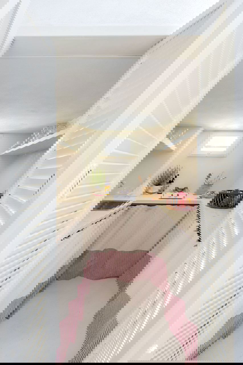 Узкая мини-кухня/кладовая в микроквартире: занавески вместо фасадов, светлая столешница и аккуратно расположенная посуда и продукты.