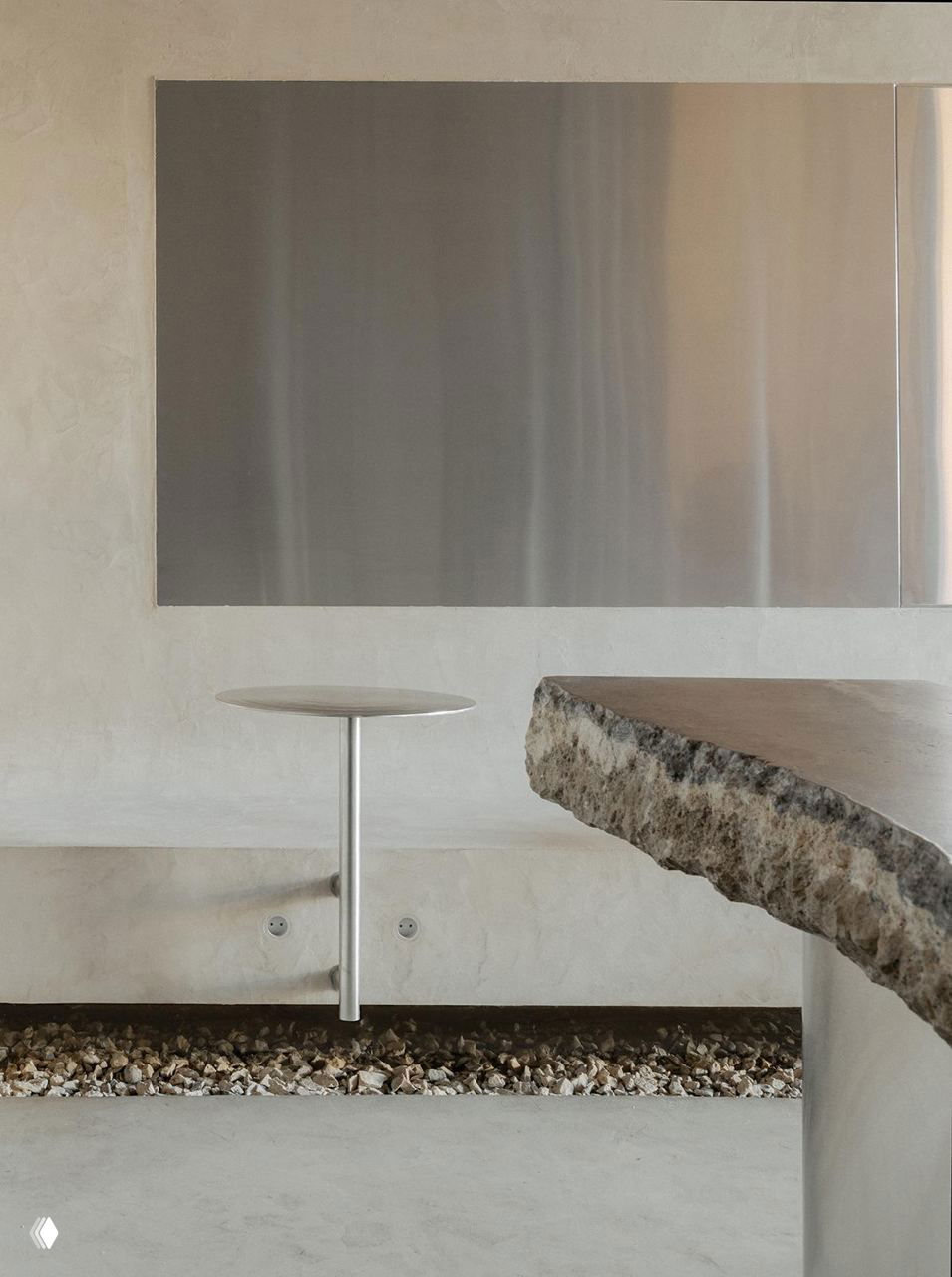 Минималистичный интерьер с низкими столиками и скамьёй из микроцемента, крупный контраст текстур между деревом и металлом в пространстве.