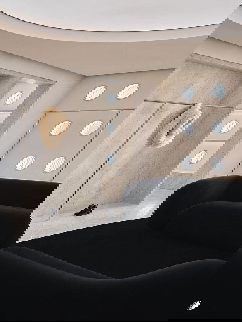 Интерьер бутика: чёрные плавные диваны на фоне светлого каррарского мрамора и ряд круглых окон, создающих мягкую атмосферу торгового пространства.