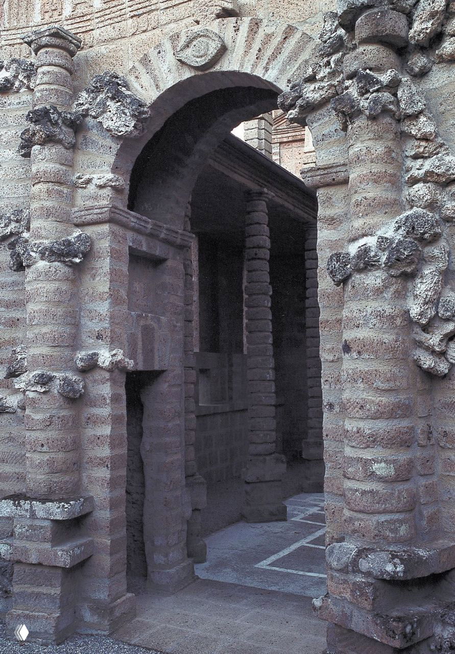 Крупный план архитектурных деталей Ла Скарцуола: арки и столбы из туфа с грубой текстурой, видна естественная эрозия и фактура камня.