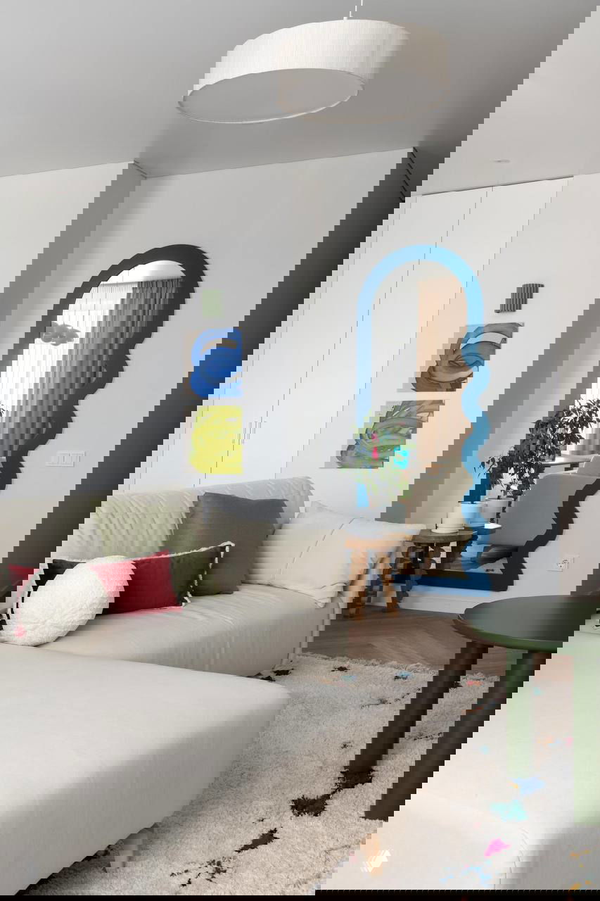 Общий вид гостиной: мягкий кремовый диван, крупный пушистый ковер с цветными акцентами, голубое волнообразное зеркало в проемe.