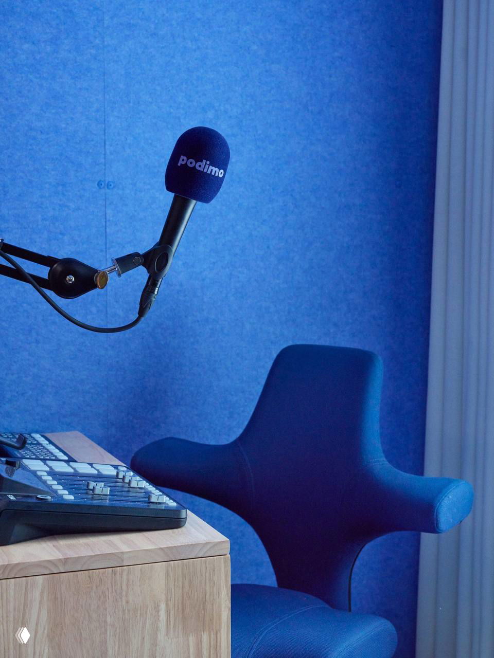 Студийный микрофон с чехлом с логотипом Podimo на фоне акустической синих панелей и необычного синего кресла со скульптурным силуэтом.