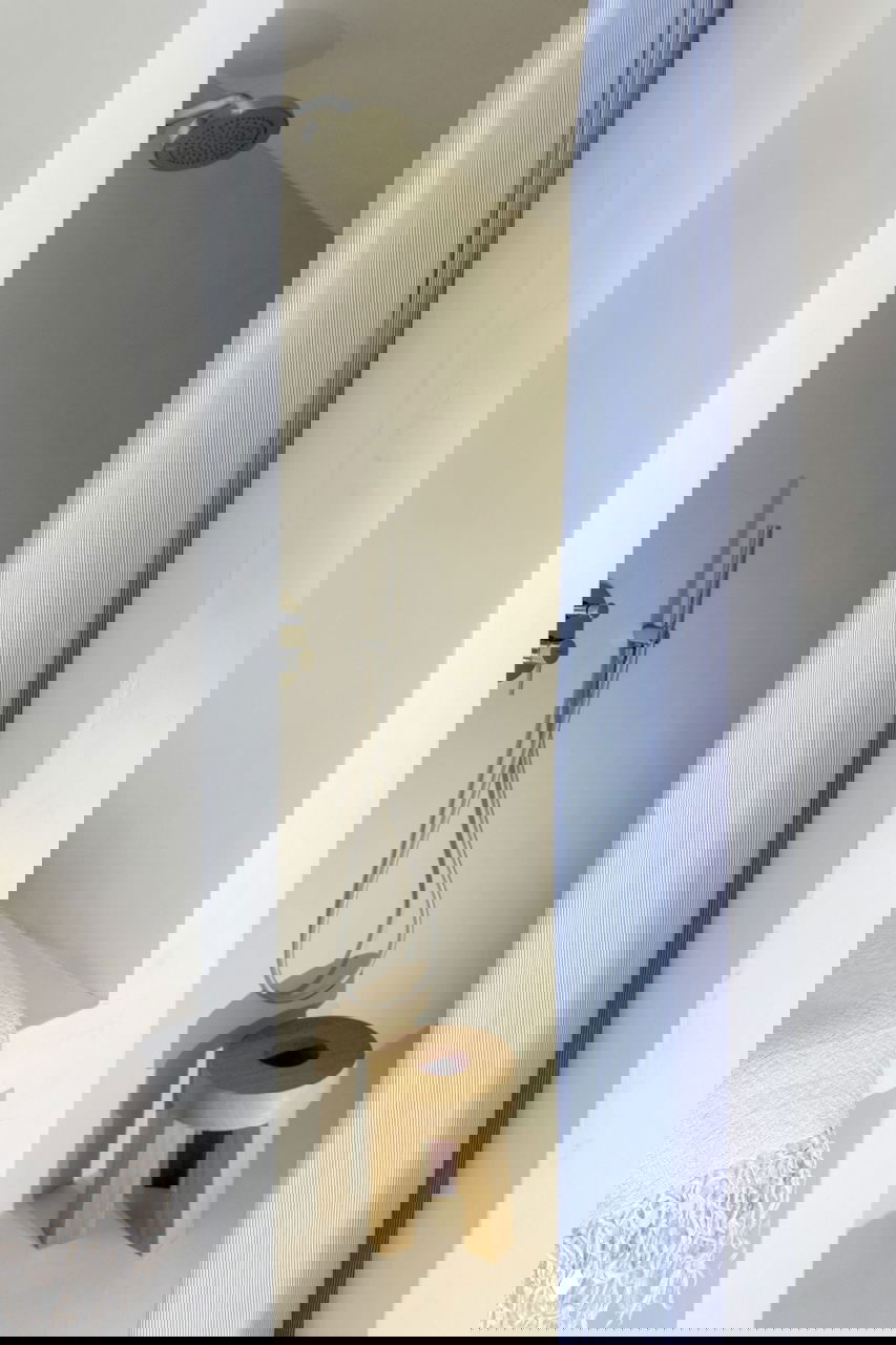 Мини-душевая ниша со скрытой лейкой, деревянный табурет и тонкая голубая шторка — пример рационального и эстетичного использования небольшого пространства.