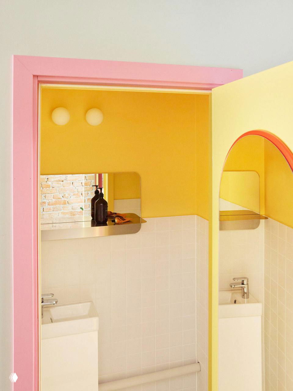 Фрагмент санузла или небольшой комнаты с розовой рамой дверного проема, стенами в желтом цвете и арочным зеркалом — контрастные пастельные акценты в интерьере.