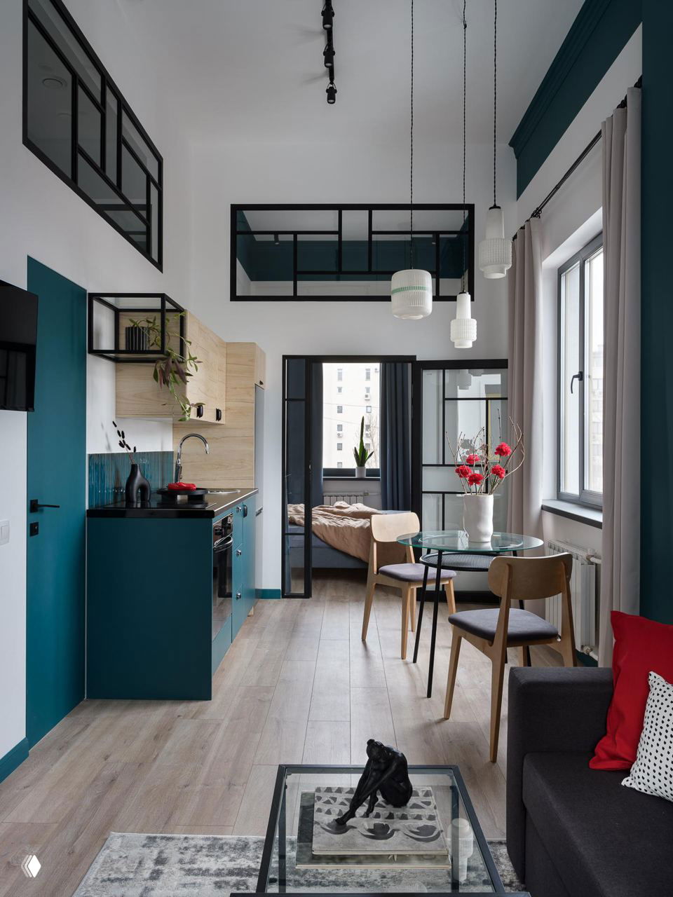 Кухня‑гостиная в 37‑м² квартире в Москве: бирюзовые кухонные фасады, тёмная столешница, стеклянные межкомнатные окна и подвесные винтажные плафоны.