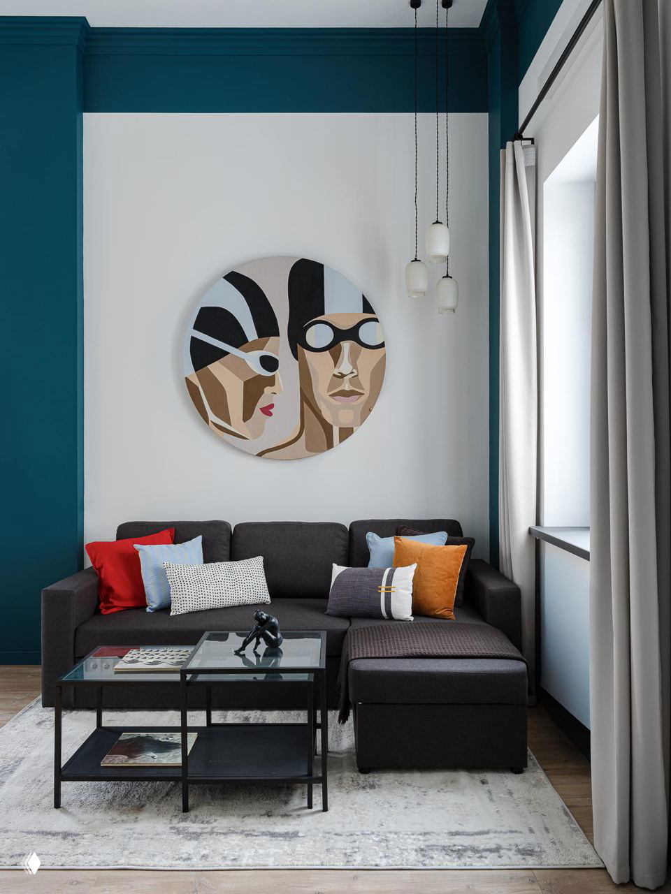 Уютная зона гостиной с тёмно‑серым диваном, яркими декоративными подушками и круглой настенной картиной на белой стене, контрастные синие акценты.