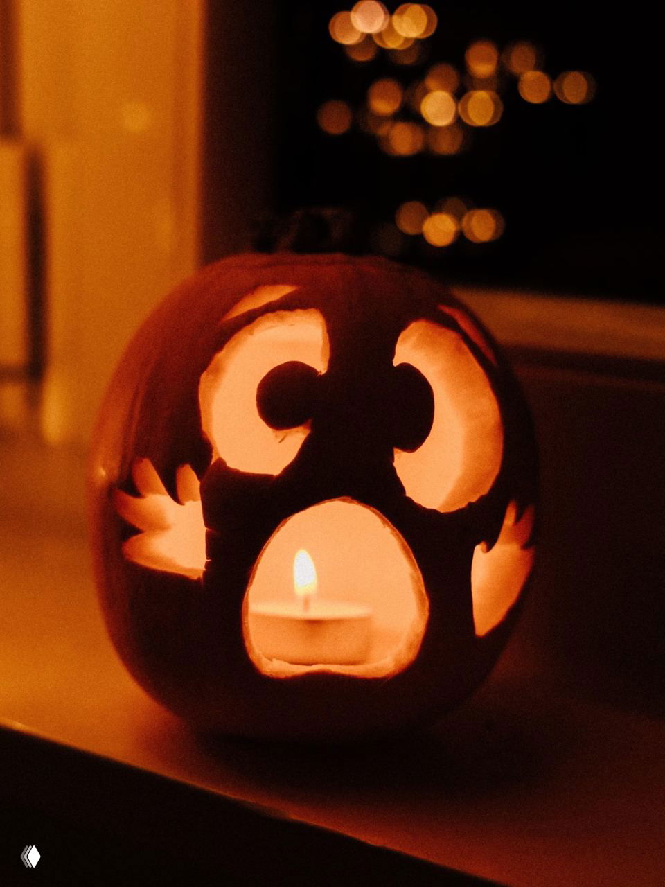 Вырезанная тыква с подсвечником внутри, крупный план; тёплое свечное сияние и размытие огней на заднем плане, фокус на свете и форме.