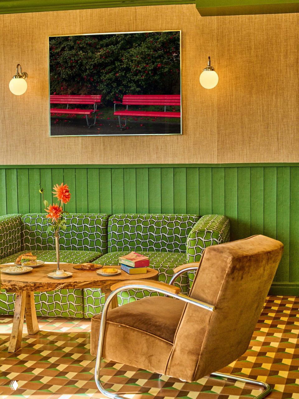 Уютный уголок ресторана: зеленый диван с узором, низкий стол из натурального дерева и велюровое кресло на фоне ритмичного пола.