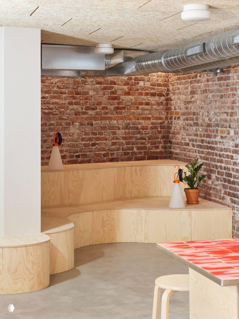 Нижний уровень с кирпичной стеной и круглыми деревянными скамьями, органично вписанными в пространство для встреч и неформального общения команды.