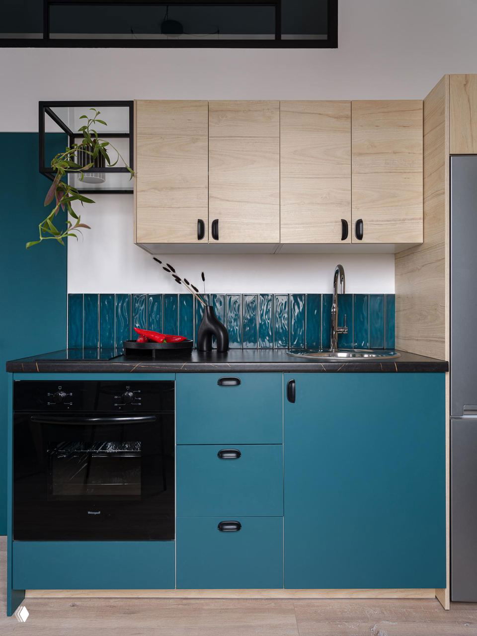 Крупный план кухонного гарнитура: бирюзовые фасады, деревянные верхние шкафы и глянцевая узкая плитка той же цветовой гаммы, чёрная фурнитура и техника.
