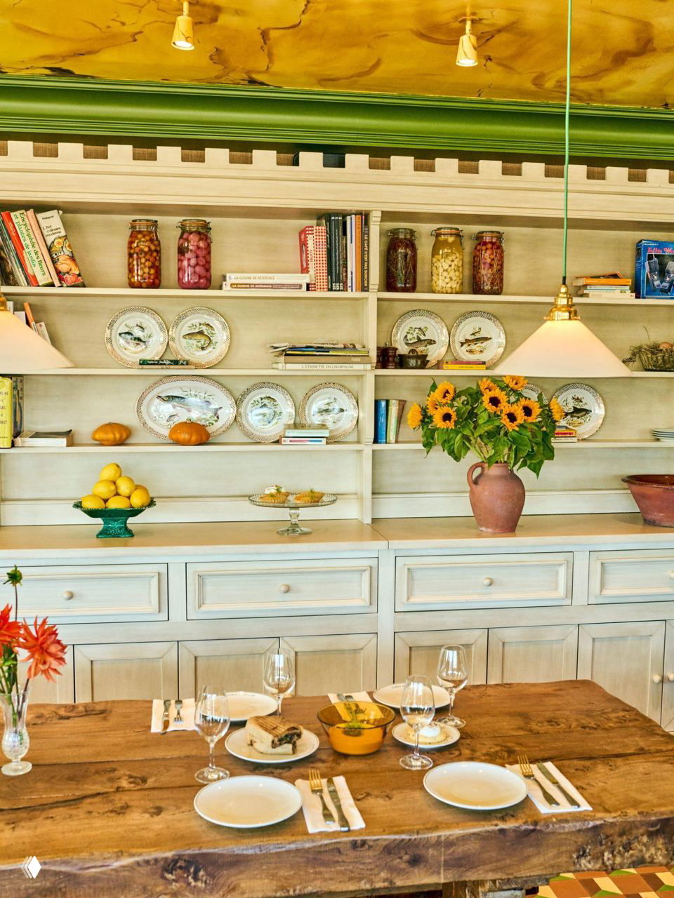 Сервированный стол у открытых полок с тарелками, заготовками в банках и вазой с подсолнухами в интерьере ресторана.